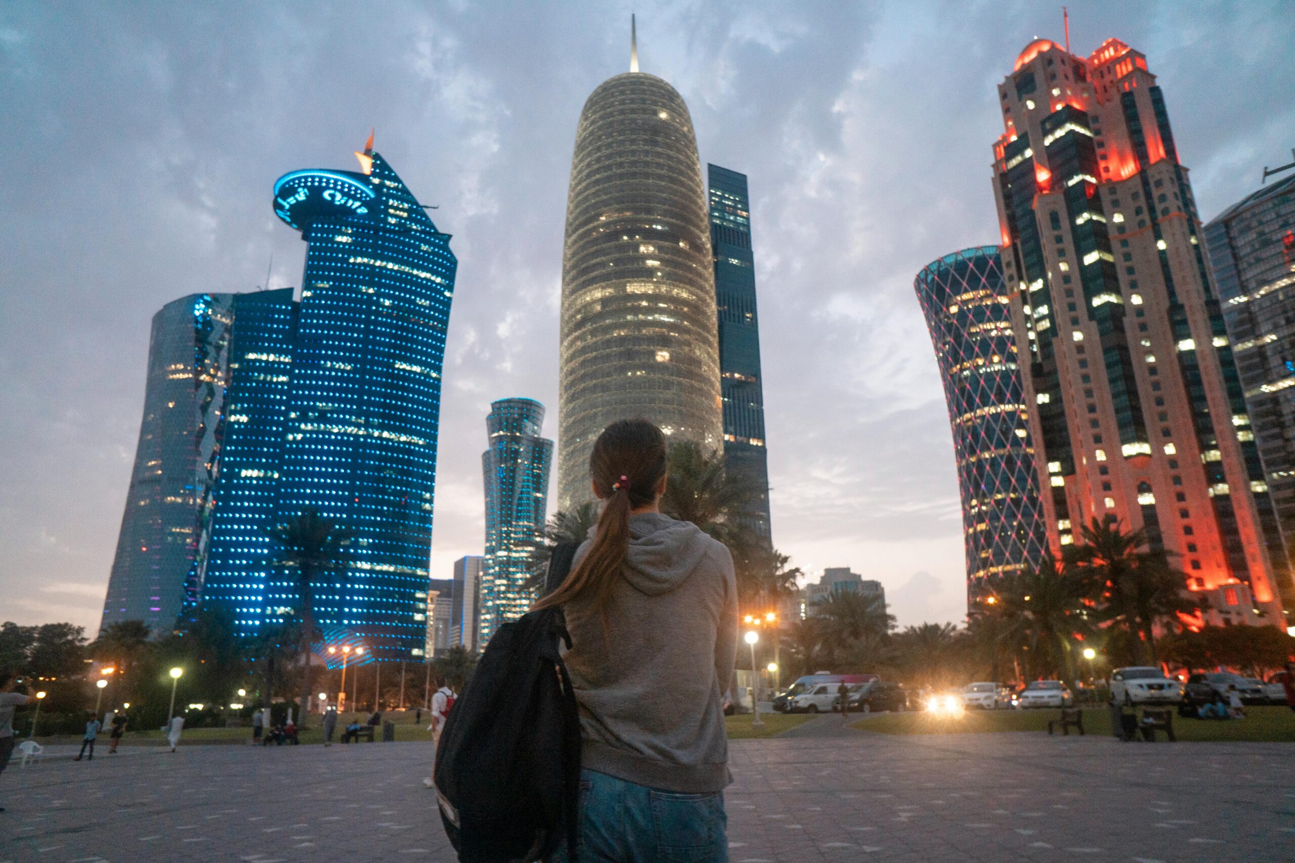 A woman gazes at the illuminated Doha skyline, highlighting modern skyscrapers at twilight.