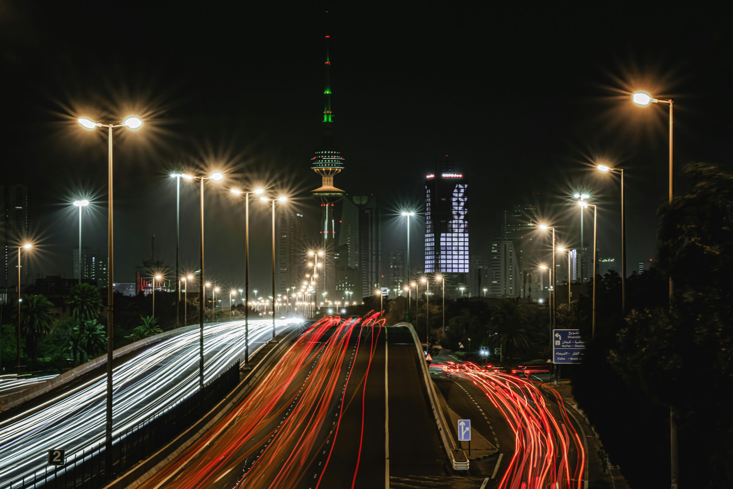 Vibrant light trails and illuminated skyline of Kuwait City at night, highlighting urban life.